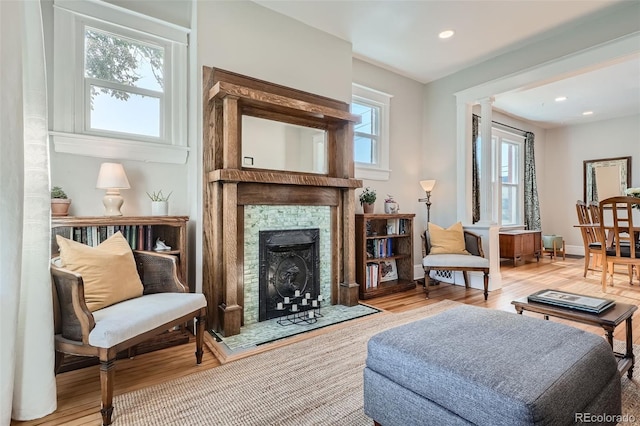 sitting room featuring light hardwood / wood-style floors, a stone fireplace, and ornate columns