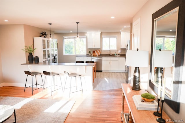 7100 Saulsbury St, Arvada, CO 80003 - kitchen featuring dishwasher, light wood-style floors, a sink, a breakfast bar, and white cabinets