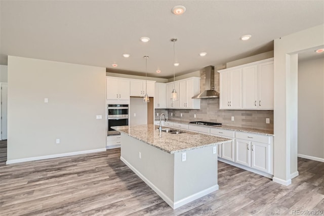 kitchen with appliances with stainless steel finishes, white cabinetry, and wall chimney range hood