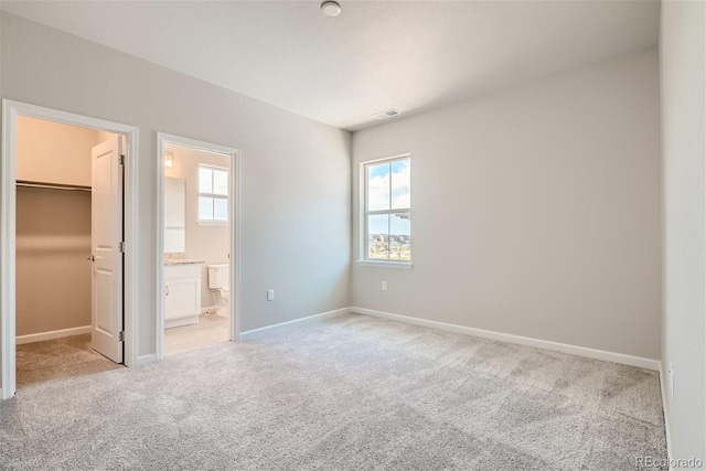 unfurnished bedroom featuring connected bathroom, multiple windows, a spacious closet, and light colored carpet