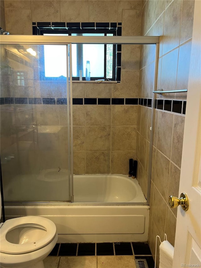 bathroom with tile patterned flooring, toilet, and combined bath / shower with glass door