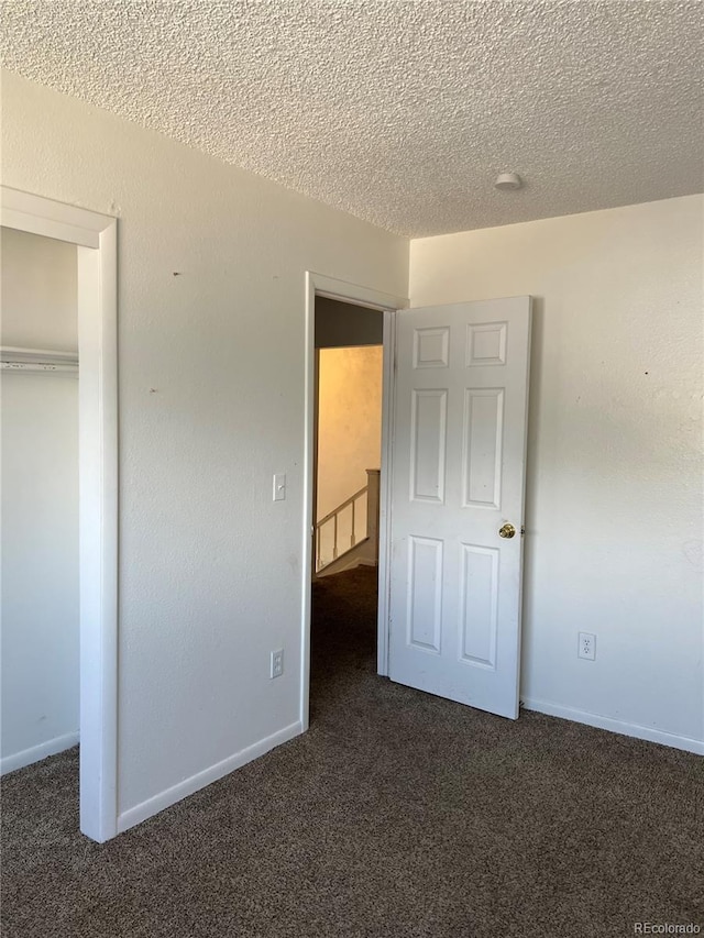 unfurnished bedroom with a textured ceiling, dark carpet, and a closet