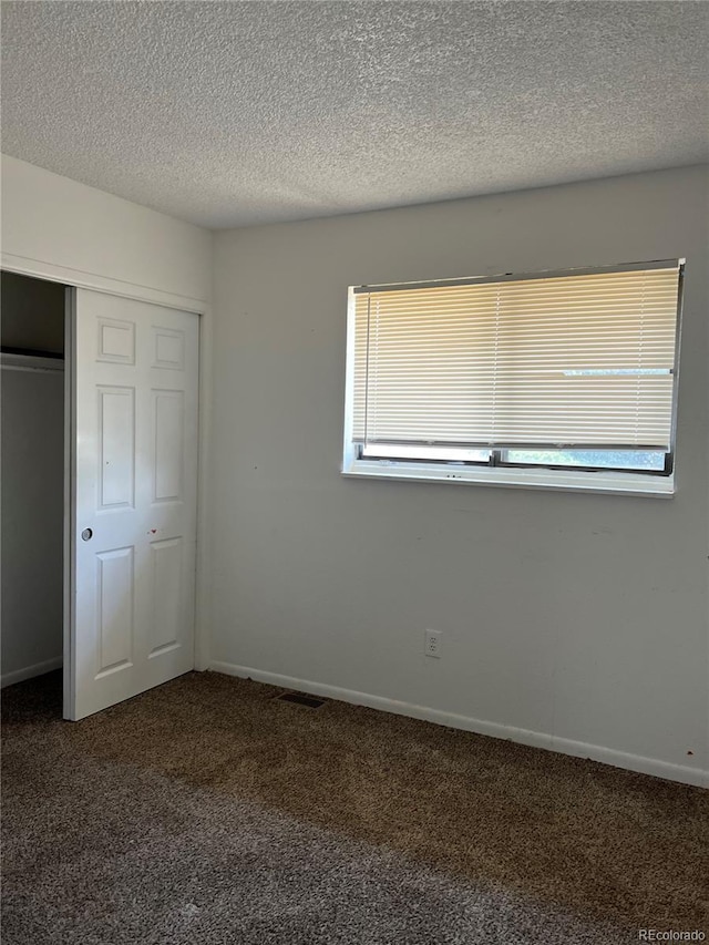 unfurnished bedroom featuring dark colored carpet, a textured ceiling, and a closet