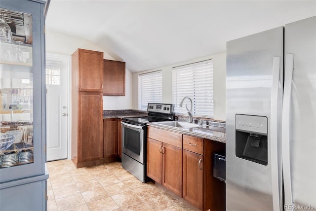 kitchen with vaulted ceiling, dark stone countertops, brown cabinetry, stainless steel appliances, and a sink