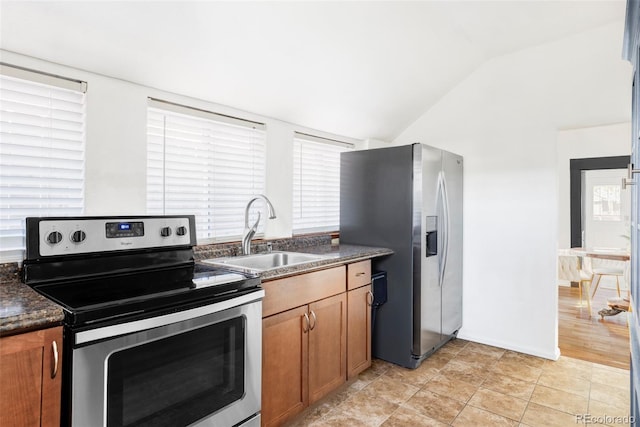 kitchen with brown cabinetry, lofted ceiling, a sink, stainless steel appliances, and dark countertops