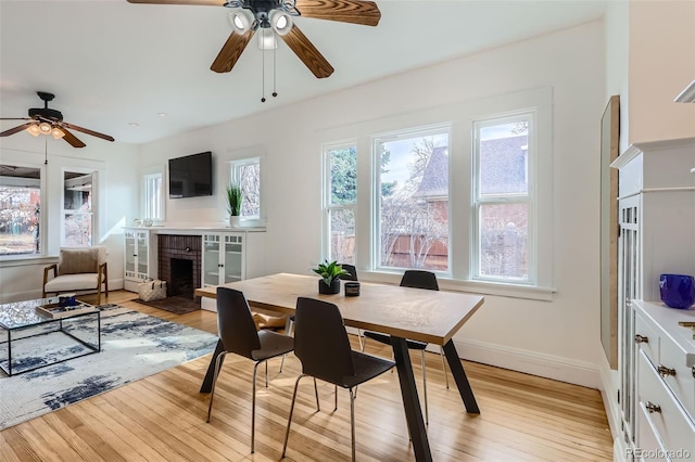 dining room with baseboards, a ceiling fan, light wood-type flooring, and a fireplace