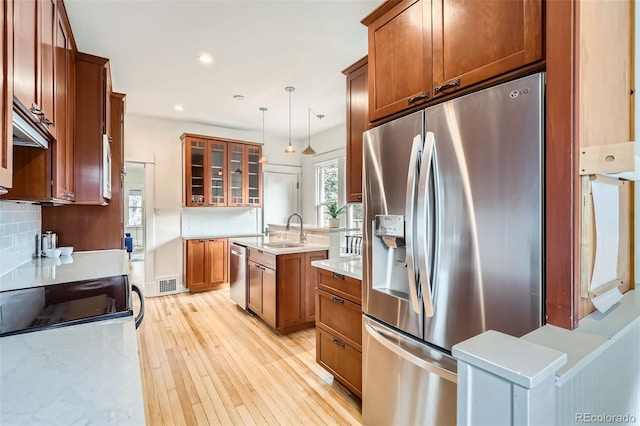 kitchen featuring light countertops, a sink, glass insert cabinets, light wood-style flooring, and appliances with stainless steel finishes