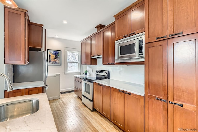 kitchen featuring stainless steel appliances, a sink, light wood-type flooring, baseboards, and decorative backsplash