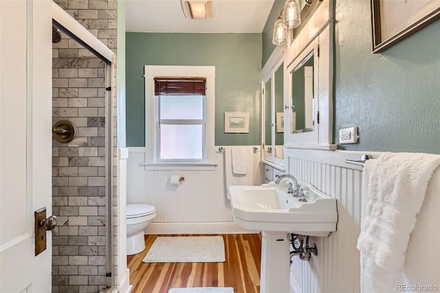 full bathroom with a shower stall, toilet, a wainscoted wall, and wood finished floors