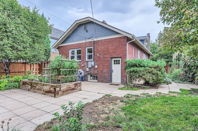 rear view of house featuring fence, a garden, brick siding, and a chimney