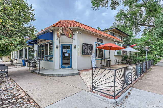 view of front of home with fence, a patio, a tiled roof, and stucco siding