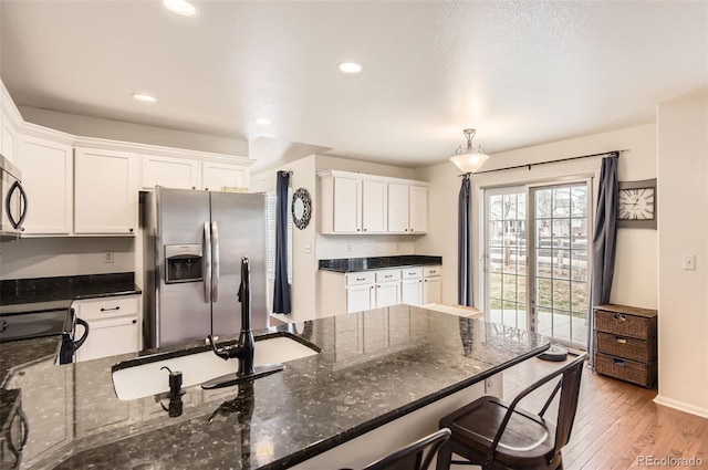 kitchen with stainless steel appliances, pendant lighting, dark stone countertops, white cabinets, and light hardwood / wood-style floors