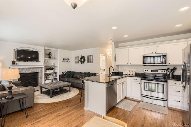 kitchen with white cabinetry, sink, stainless steel appliances, a premium fireplace, and kitchen peninsula