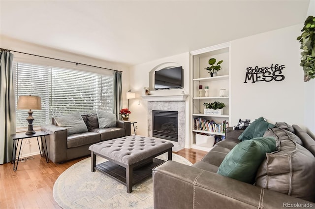 living room with built in shelves, a premium fireplace, and wood-type flooring