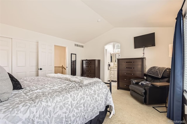 bedroom with ensuite bath, a closet, light colored carpet, and vaulted ceiling