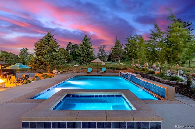 5727 Colorow Dr, Morrison, CO 80465 - pool at dusk with an outdoor pool, an in-ground hot tub, a patio area, and view of wooded area
