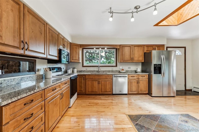 kitchen with a sink, brown cabinetry, stainless steel appliances, and light wood-type flooring