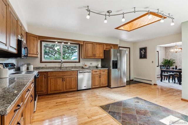 kitchen with appliances with stainless steel finishes, baseboard heating, a sink, brown cabinetry, and light wood-style flooring