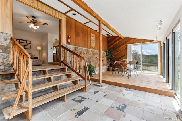 stairway featuring stone tile floors, a ceiling fan, wood walls, and vaulted ceiling