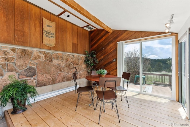 dining room with light wood-type flooring, vaulted ceiling, and wood walls