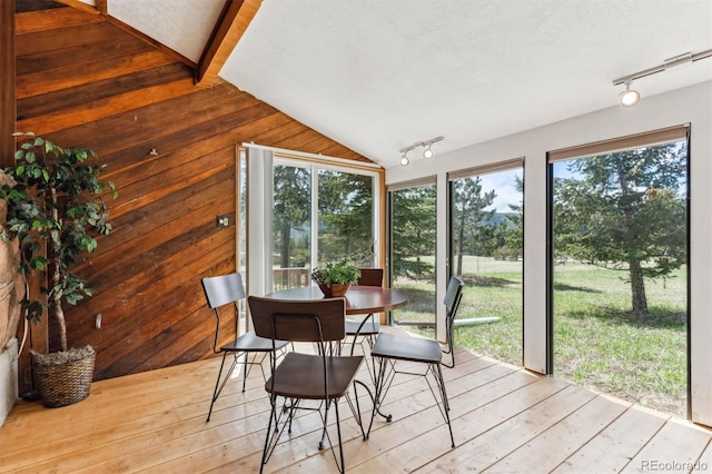 sunroom featuring wood walls, track lighting, a wooden deck, and lofted ceiling