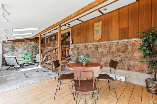 dining area with stairs, wooden walls, a skylight, and wood-type flooring