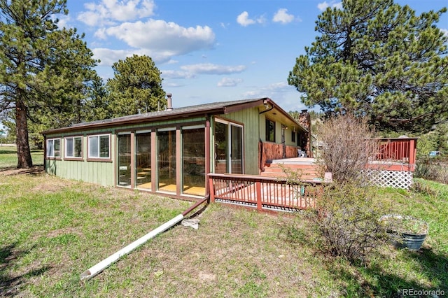 back of house featuring a lawn, a deck, a chimney, and a sunroom