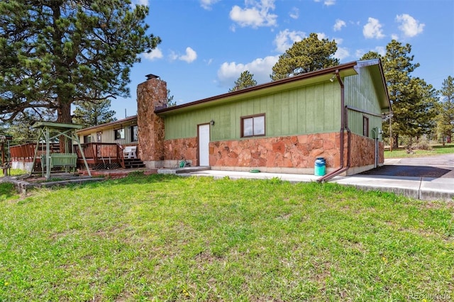 rear view of property with a lawn, a wooden deck, a chimney, and stone siding