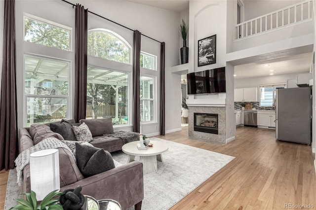 living room featuring light wood finished floors, a high ceiling, a tile fireplace, and baseboards