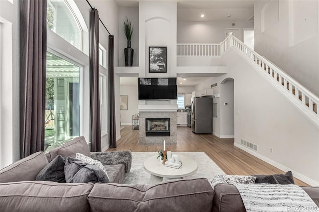 living area featuring a high ceiling, light wood-type flooring, baseboards, a fireplace, and arched walkways
