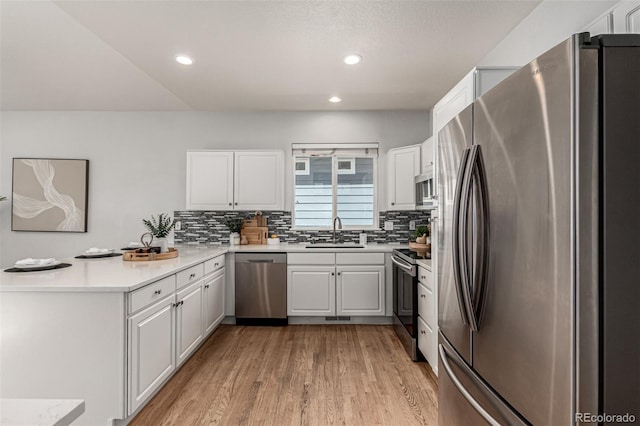kitchen featuring stainless steel appliances, a peninsula, a sink, decorative backsplash, and light wood-style floors