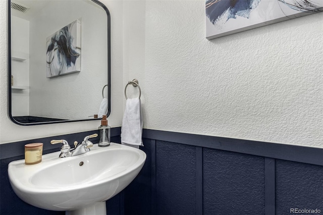 bathroom with a textured wall, a sink, and wainscoting