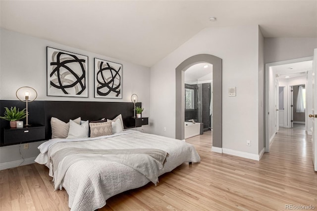 bedroom with vaulted ceiling, arched walkways, light wood-style floors, and baseboards