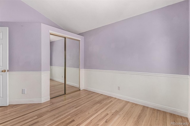unfurnished bedroom featuring wood finished floors, a closet, lofted ceiling, and baseboards