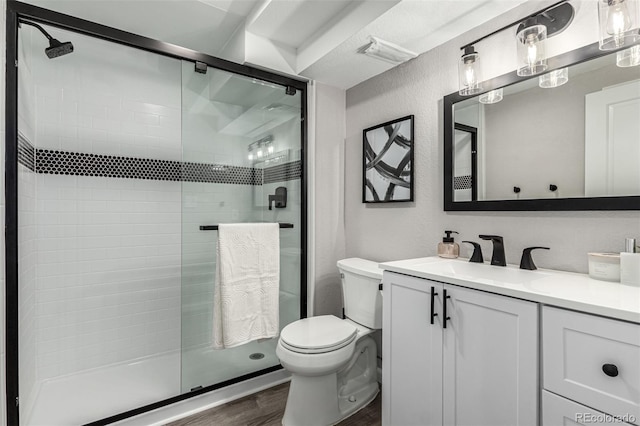 bathroom with wood finished floors, toilet, a stall shower, vanity, and a textured wall