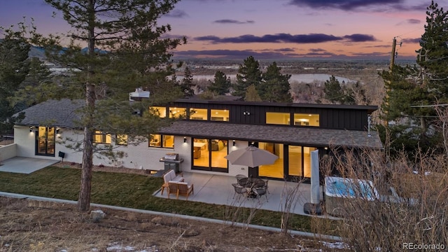 back house at dusk with a patio and a lawn