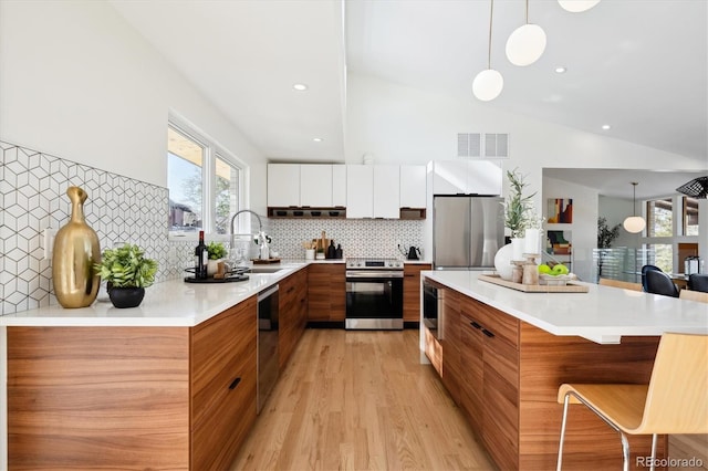 kitchen featuring appliances with stainless steel finishes, decorative light fixtures, white cabinetry, lofted ceiling, and a kitchen breakfast bar