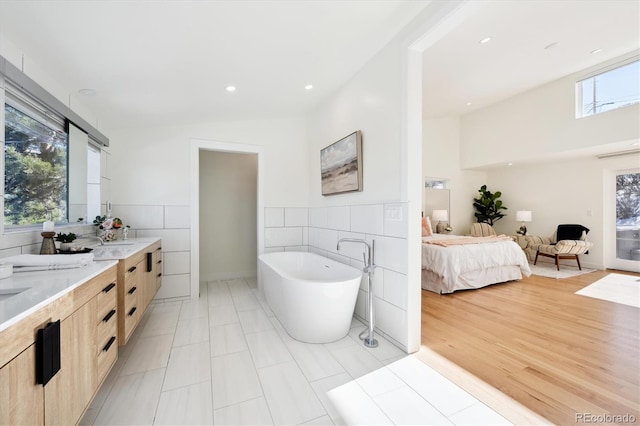 bathroom featuring vanity, a bath, tile walls, and a wealth of natural light