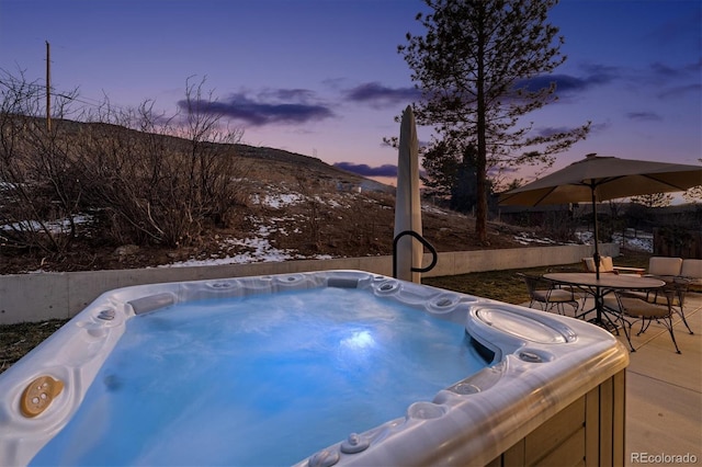 pool at dusk featuring a hot tub, a patio, and a mountain view