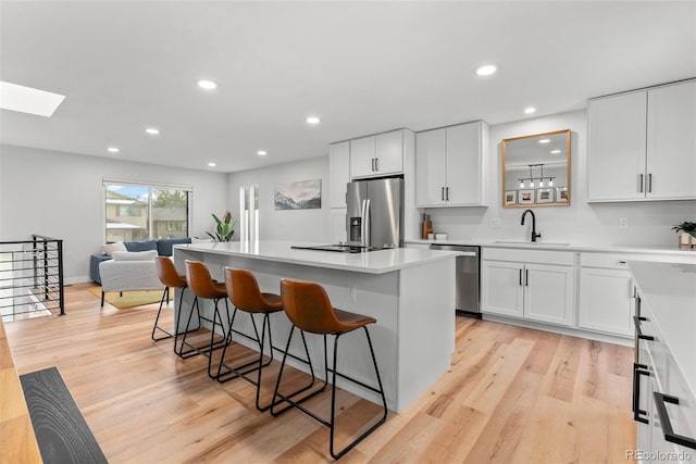 kitchen featuring stainless steel appliances, a breakfast bar, a kitchen island, sink, and white cabinets