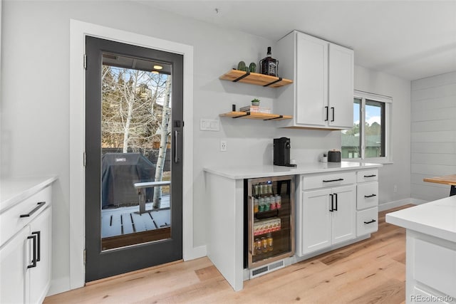 bar with white cabinets, beverage cooler, and light hardwood / wood-style flooring