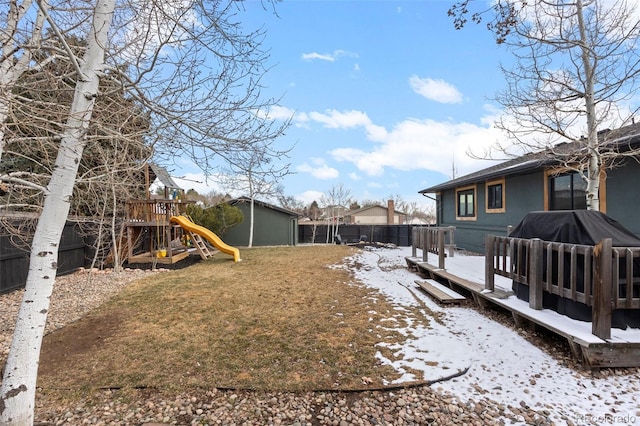 yard layered in snow with a playground and a deck