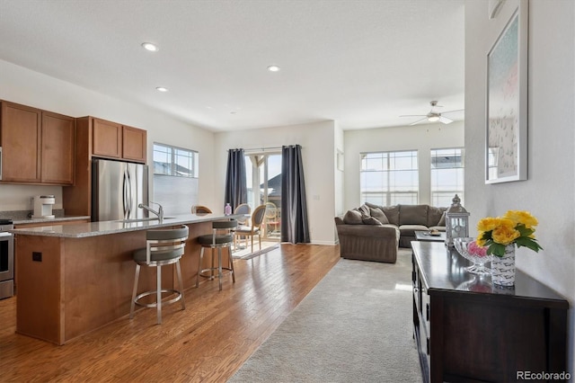 kitchen featuring ceiling fan, appliances with stainless steel finishes, a center island with sink, light hardwood / wood-style floors, and a kitchen bar