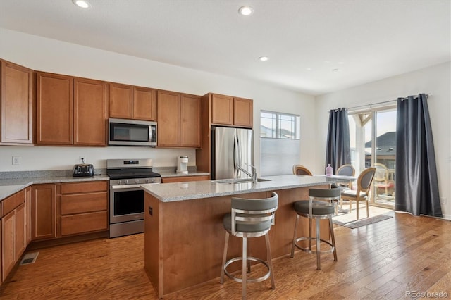 kitchen with a breakfast bar area, light stone counters, light hardwood / wood-style flooring, appliances with stainless steel finishes, and an island with sink