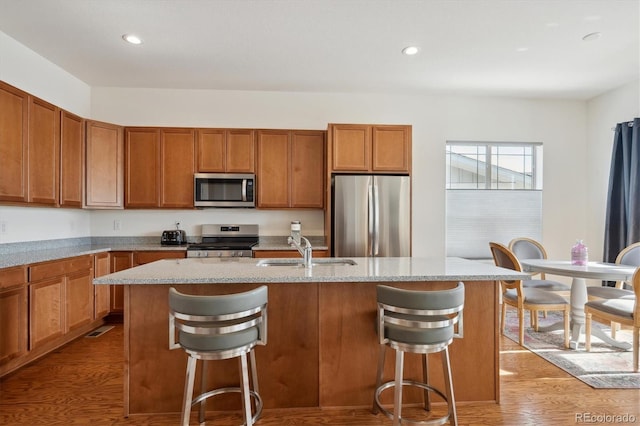 kitchen featuring sink, light hardwood / wood-style flooring, appliances with stainless steel finishes, a kitchen breakfast bar, and an island with sink