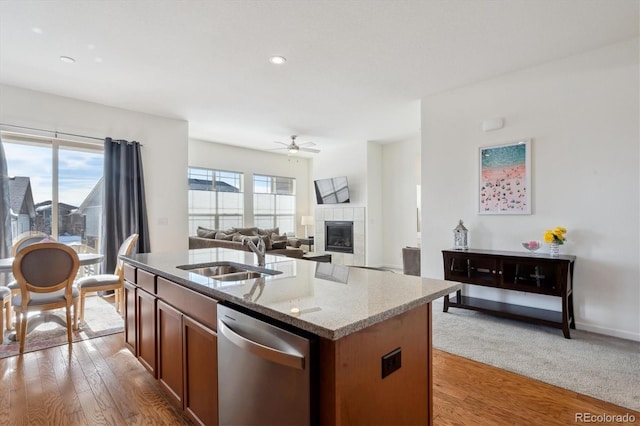 kitchen featuring sink, a fireplace, light hardwood / wood-style floors, an island with sink, and stainless steel dishwasher