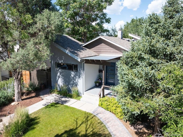 view of front facade with a chimney, stucco siding, a front lawn, and roof with shingles