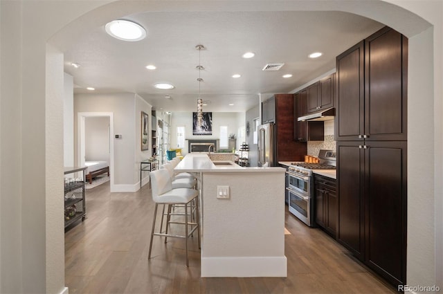 kitchen featuring visible vents, under cabinet range hood, open floor plan, a breakfast bar area, and appliances with stainless steel finishes