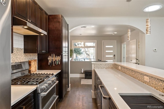 kitchen featuring dark brown cabinetry, light countertops, arched walkways, stainless steel appliances, and dark wood-style flooring