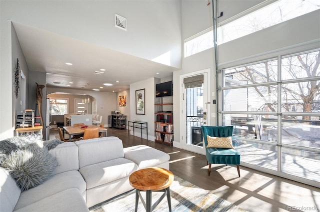 living area featuring visible vents, baseboards, a high ceiling, wood finished floors, and arched walkways